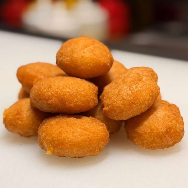 A pile of golden-brown, fried dough balls, possibly hushpuppies or donut holes, on a white surface.