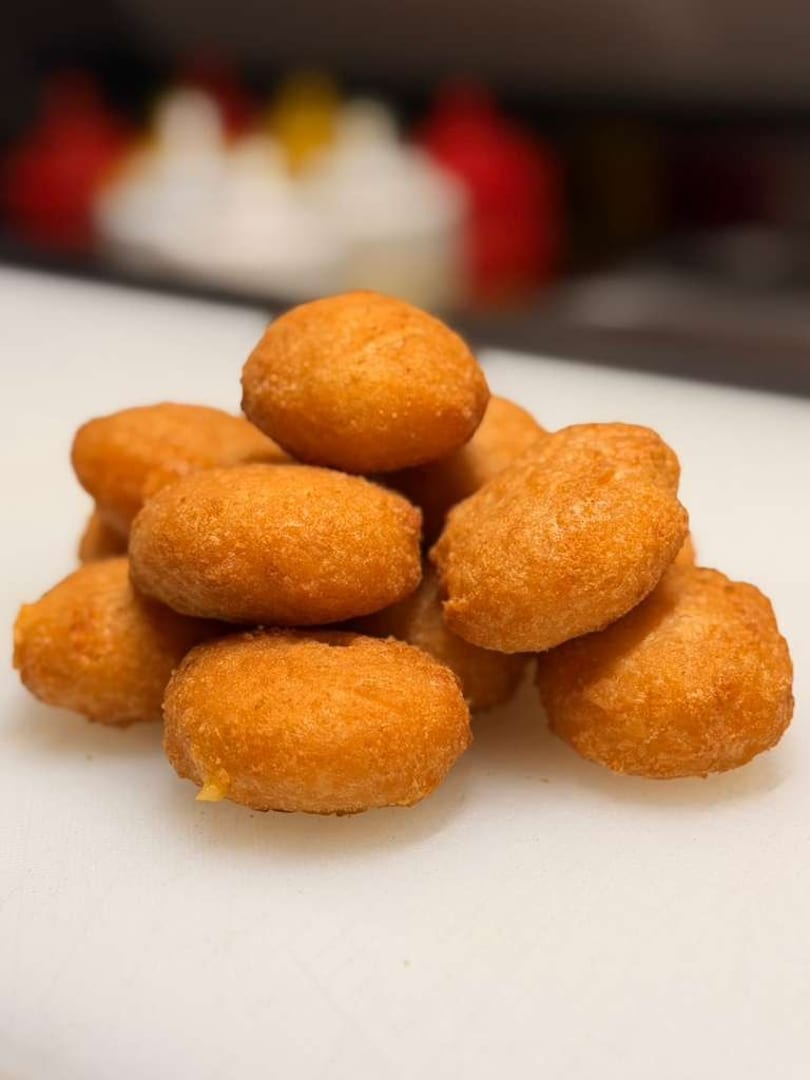 A pile of golden-brown, fried dough balls, possibly hushpuppies or donut holes, on a white surface.