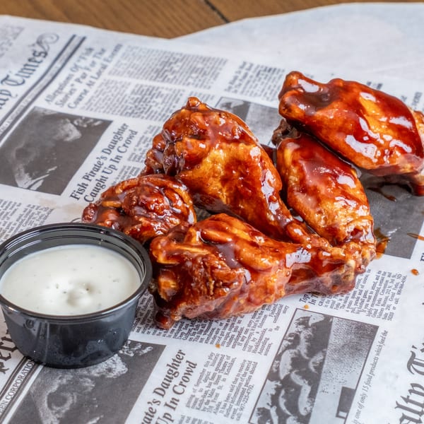 Glazed chicken wings served with ranch dipping sauce on newspaper-style restaurant paper.