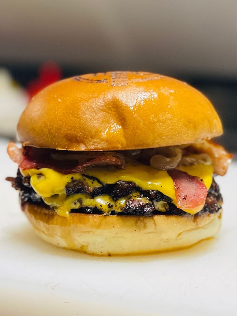 Close-up of a double cheeseburger with bacon, melted cheese, and caramelized onions on a brioche bun.