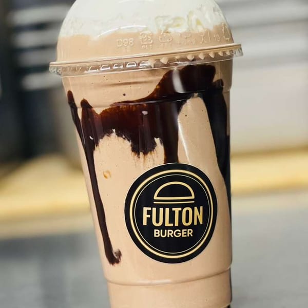 Chocolate milkshake with whipped cream and chocolate drizzle in a Fulton Burger branded cup.