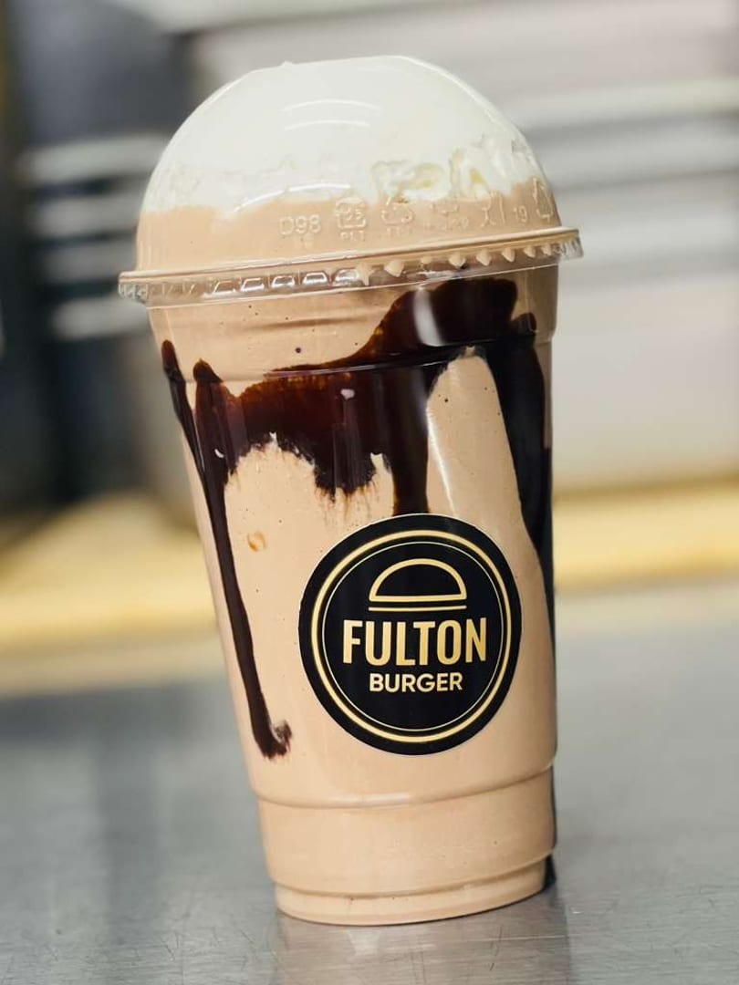Chocolate milkshake with whipped cream and chocolate drizzle in a Fulton Burger branded cup.
