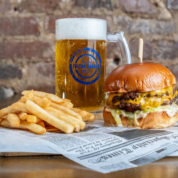 Double cheeseburger with lettuce and sauce, golden fries, and a pint of beer on newspaper-style table paper.