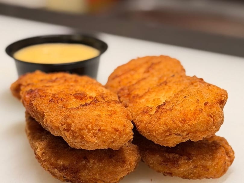 Crispy golden-brown chicken tenders piled on a white surface with a small cup of dipping sauce.