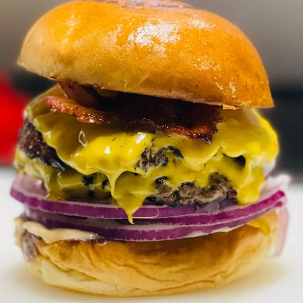 Close-up of a double cheeseburger with bacon, melted cheese, and red onion on a brioche bun.