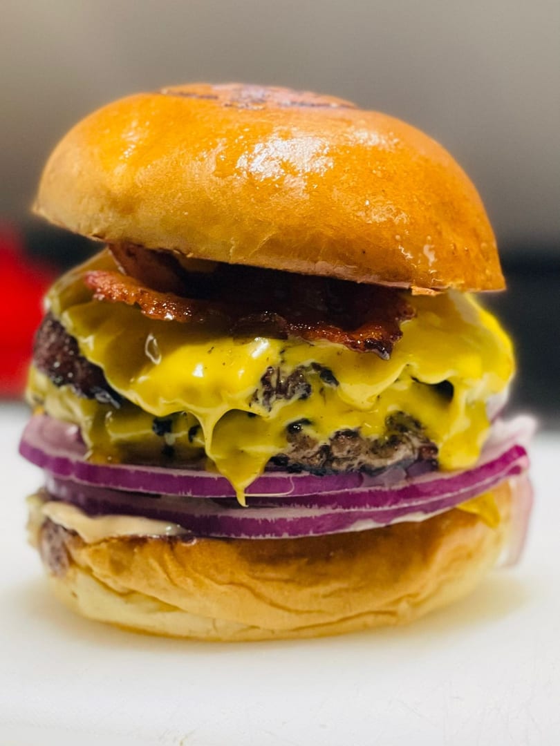 Close-up of a double cheeseburger with bacon, melted cheese, and red onion on a brioche bun.