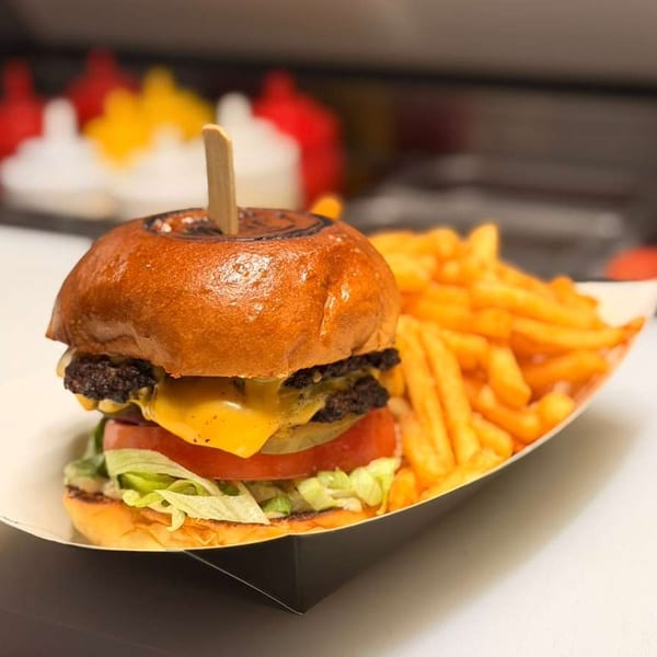A double cheeseburger with lettuce, tomato, and pickles, served with a side of golden french fries.