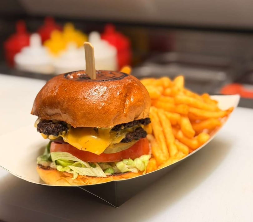 A double cheeseburger with lettuce, tomato, and pickles, served with a side of golden french fries.