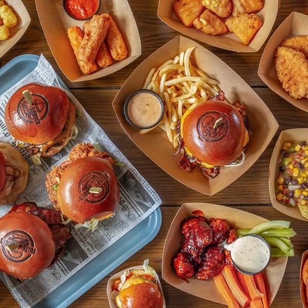 An overhead view of a wooden table laden with various burgers, fries, chicken tenders, and appetizers.