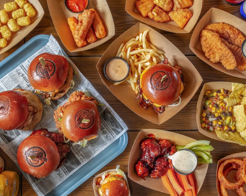 An overhead view of a wooden table laden with various burgers, fries, chicken tenders, and appetizers.