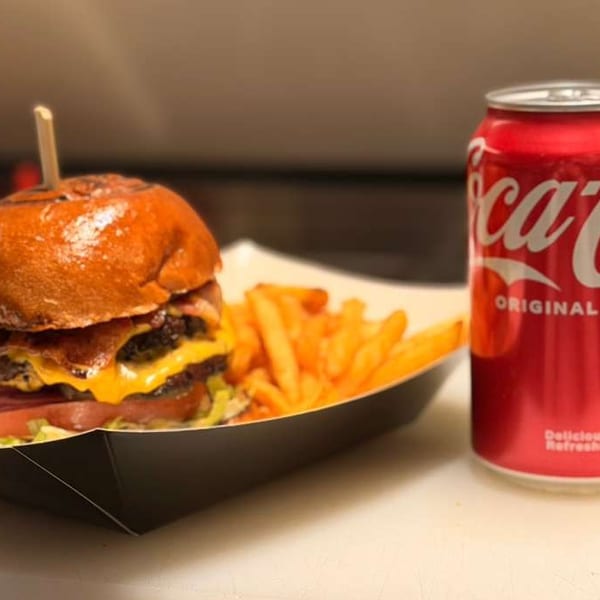 A double cheeseburger with bacon, lettuce, tomato, and fries, next to a Coca-Cola can.