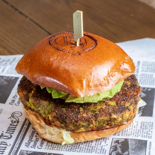 Close-up of a veggie burger with a glossy bun, lettuce, avocado, and a textured vegetable patty on newspaper-style paper.